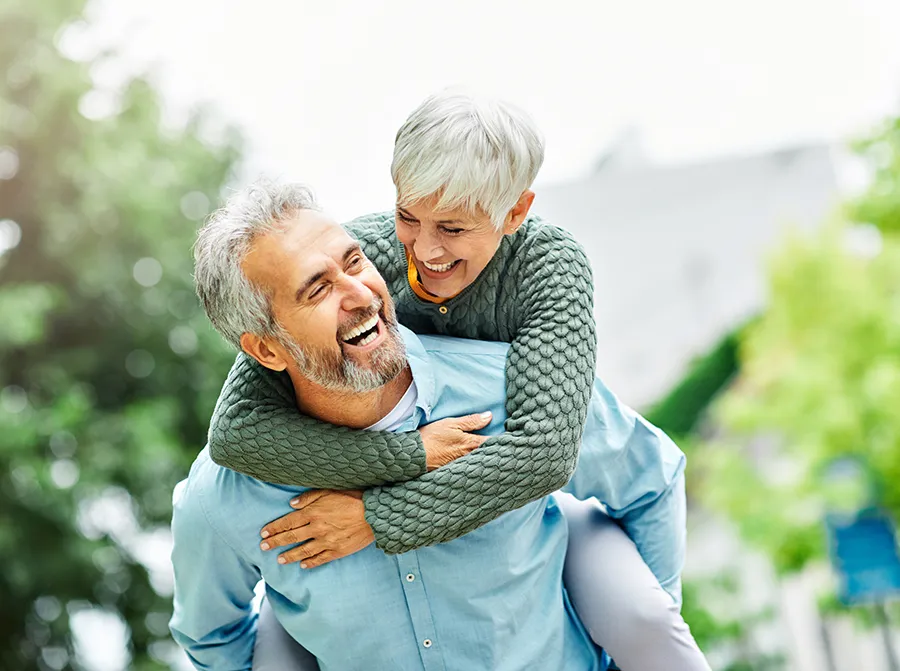 playful older couple in mid 60s man is giving woman a piggy back ride